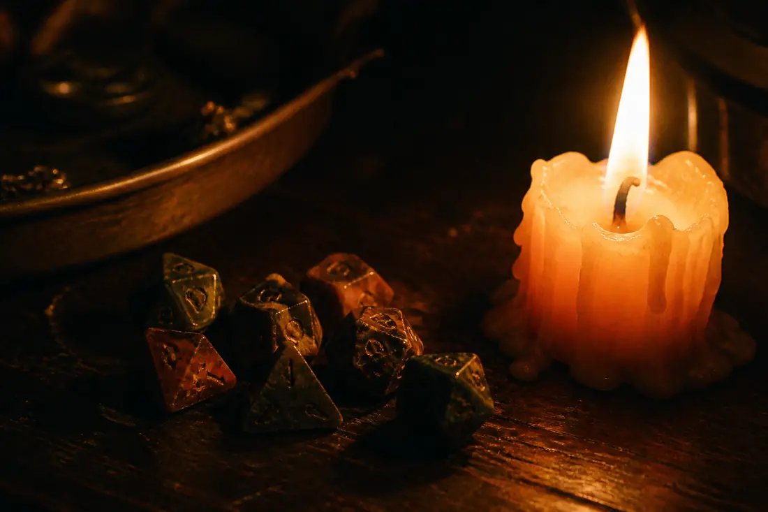 Worn polyhedral dice beside a guttering candle on dark wood