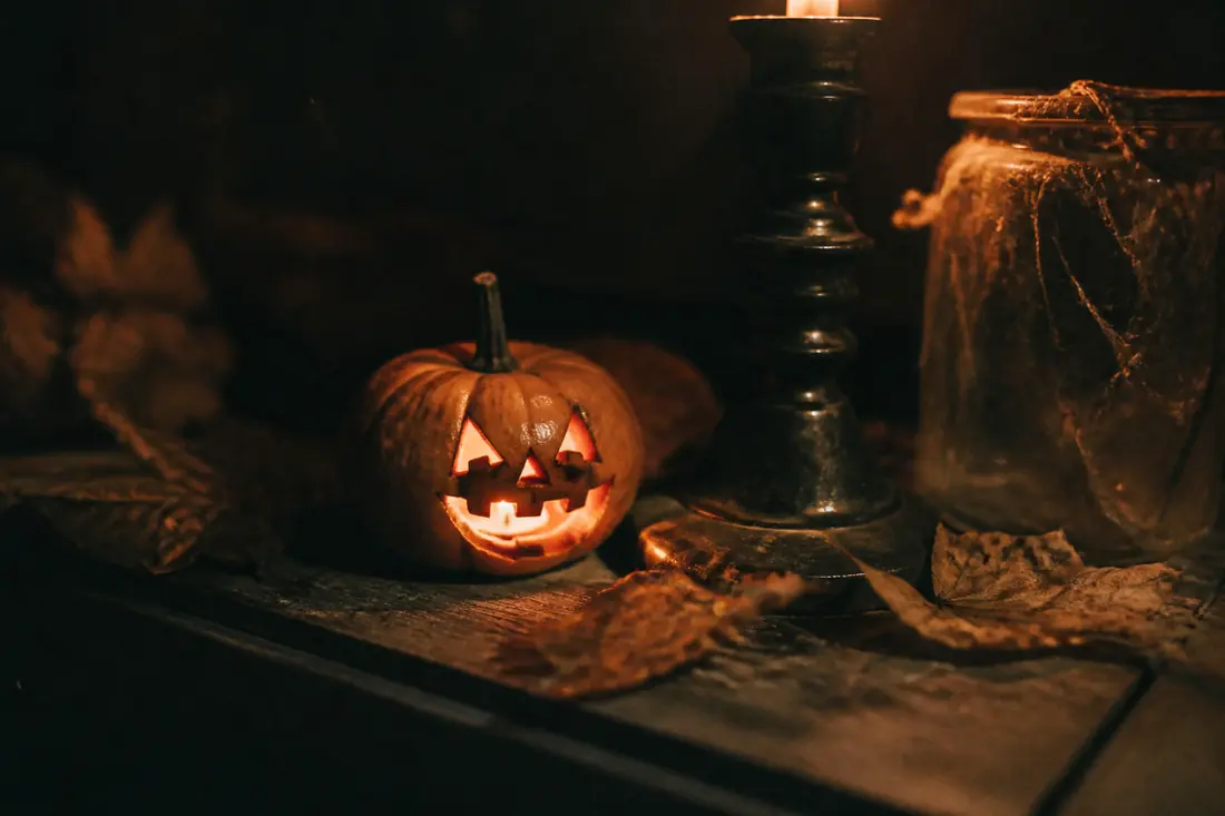 A small carved pumpkin lit by a candle on weathered dark wood